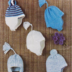 Könnte beinhalten: Fünf gestrickte Baby-Mützen in Blau und Weiß mit Ohrenklappen. Die Mützen haben verschiedene Texturen und Stile, darunter einen Bommel, Quasten und Zopfmuster.