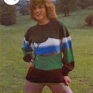 May include: A woman wearing a green, blue, white and brown striped jumper with a landscape design. The jumper has a dark brown neckline and long sleeves.