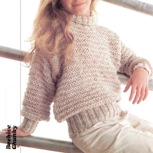 Könnte beinhalten: Ein beiger Strickpullover mit einem Wabenmuster. Der Pullover hat einen runden Ausschnitt und lange Ärmel. Der Pullover wird von einer jungen Person getragen, die eine weiße Hose trägt. Der Text "Odpiens Fast-Fun-Fashion" ist in der oberen linken Ecke des Bildes sichtbar. Der Text "56-81 cm 22-32 in Childs sizes included" ist in der oberen rechten Ecke des Bildes sichtbar.