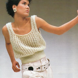 May include: A white crocheted tank top with a trellis lace pattern and buttoned shoulder straps. The top has a low back neckline. The model is wearing white trousers with a black and white spotted belt. The text "30 - 40 Chest" is printed on the bottom right corner of the image.