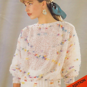 May include: A cream-coloured, open-weave knitted sweater with colourful flecks. The sweater has a crew neck and long sleeves with a ribbed cuff. The text "Knit with Odd Needles" is in a red box. The text "LIMITED EDITION No. 100" is in a red box.