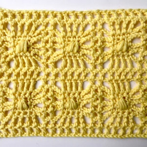 May include: A close-up of a yellow crocheted fabric with a repeating pattern of open circles and small knots. The fabric has a delicate and airy texture.
