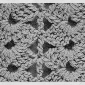 May include: Close-up of a crocheted fabric with a repeating pattern of small flowers. The fabric is a light gray color and has a textured surface.