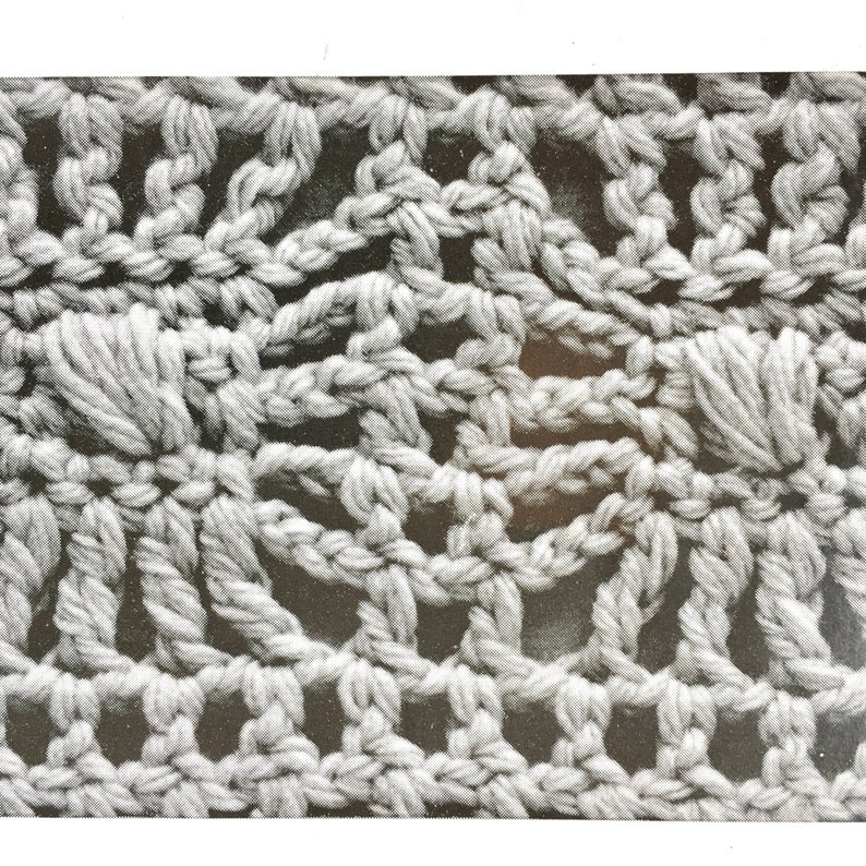 May include: Close-up of a crocheted fabric with a repeating pattern of small flowers. The fabric is a light grey colour and has a soft, textured appearance.