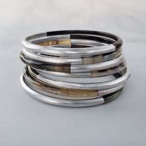May include: A stack of silver and brown bangles. The bangles are made of horn and have a silver finish.