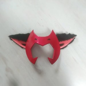 May include: Red headband with black fur cat ears. The headband has a pointed, heart-shaped design.