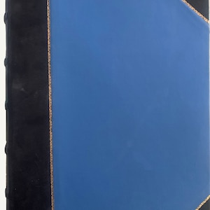 May include: A blue leather-bound book with a black spine and gold accents. The book is closed and the cover is smooth.
