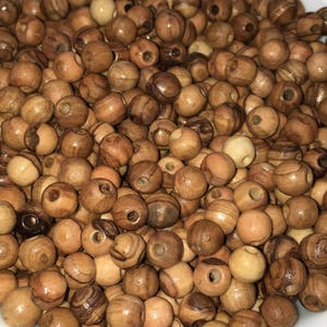 May include: A bowl filled with natural wood beads. The beads are round and have a light brown color with darker brown streaks.