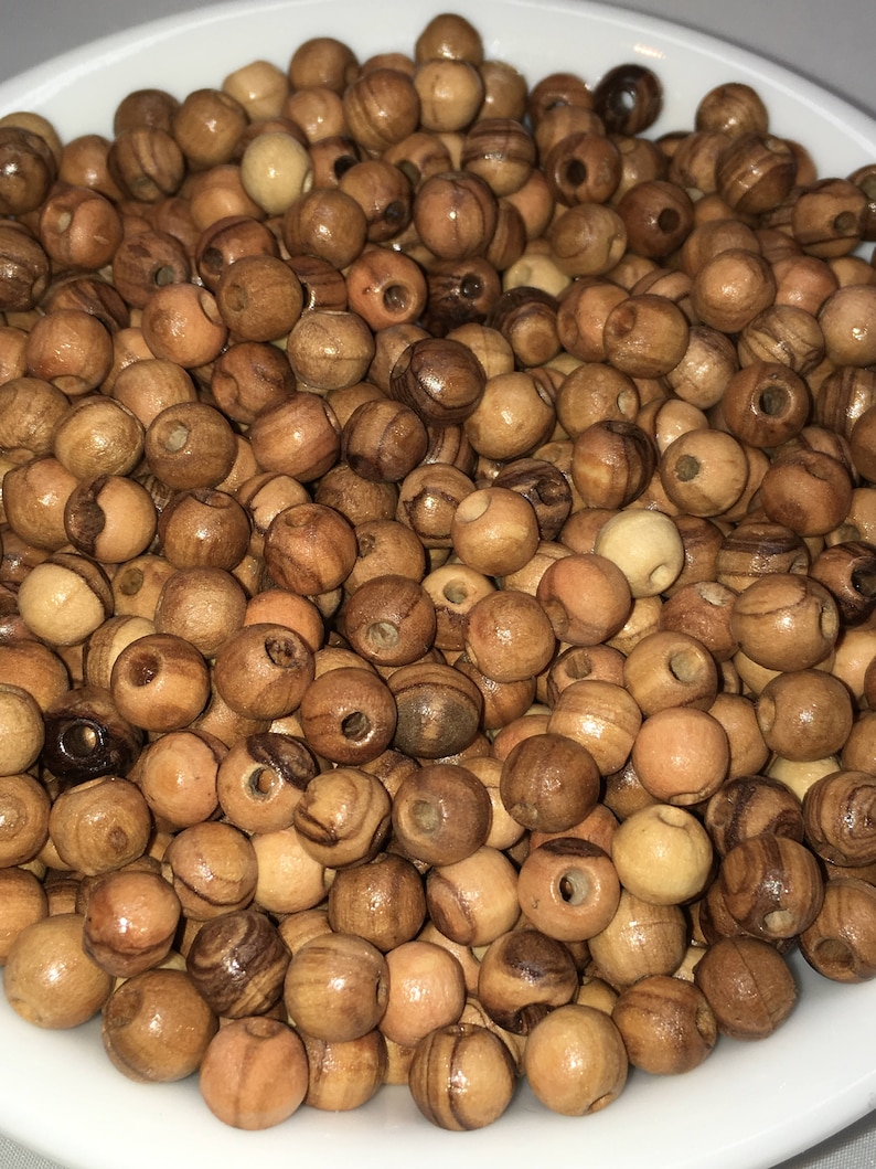 May include: A bowl filled with natural wood beads. The beads are round and have a light brown color with darker brown streaks.