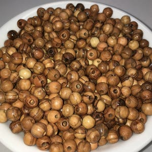 May include: A white bowl filled with a large quantity of small, round, wooden beads. The beads are a light brown color with darker brown streaks.
