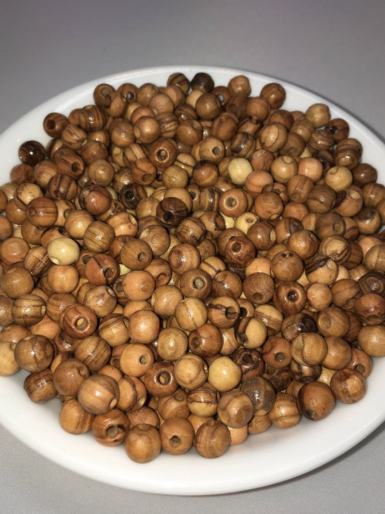 May include: A white bowl filled with a large quantity of small, round, wooden beads. The beads are a light brown color with darker brown streaks.