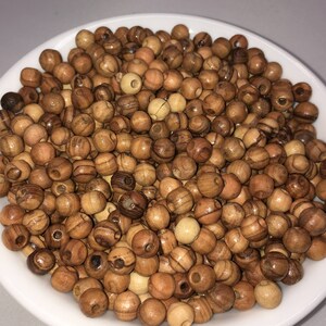 May include: A white bowl filled with a large quantity of small, round, wooden beads. The beads are a light brown color with darker brown streaks.