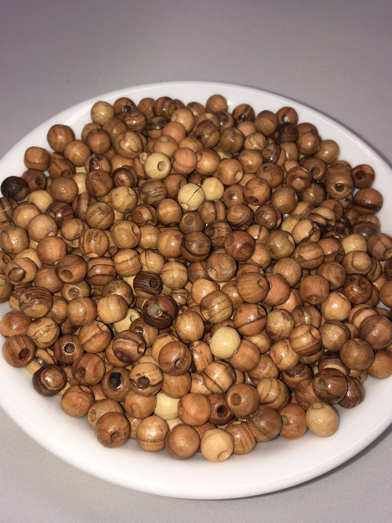 May include: A white bowl filled with a large quantity of small, round, wooden beads. The beads are a light brown color with darker brown streaks.