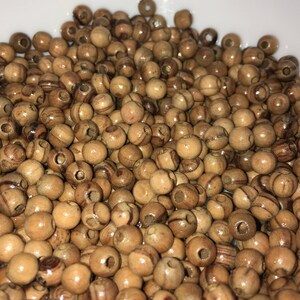May include: A bowl filled with a large quantity of natural wood beads. The beads are round and have a light brown color with darker brown streaks.