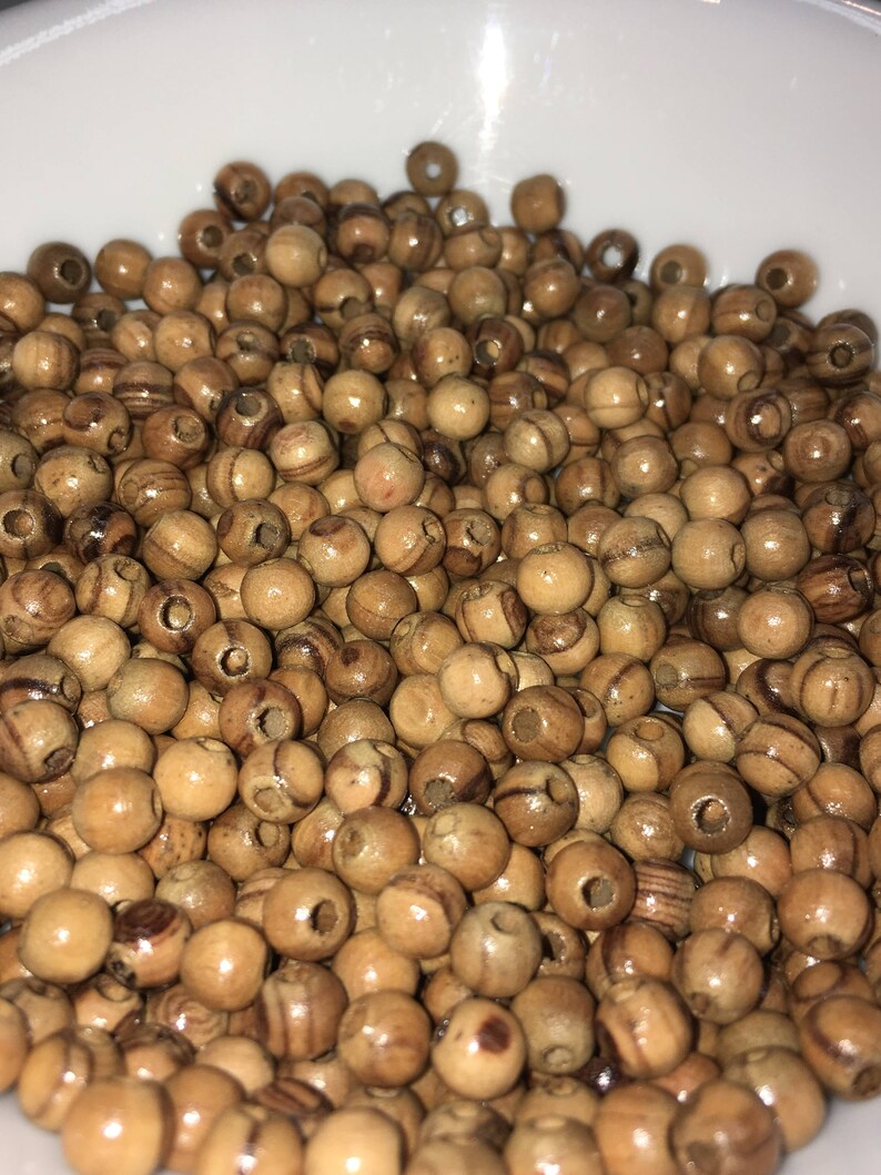 May include: A bowl filled with a large quantity of natural wood beads. The beads are round and have a light brown color with darker brown streaks.