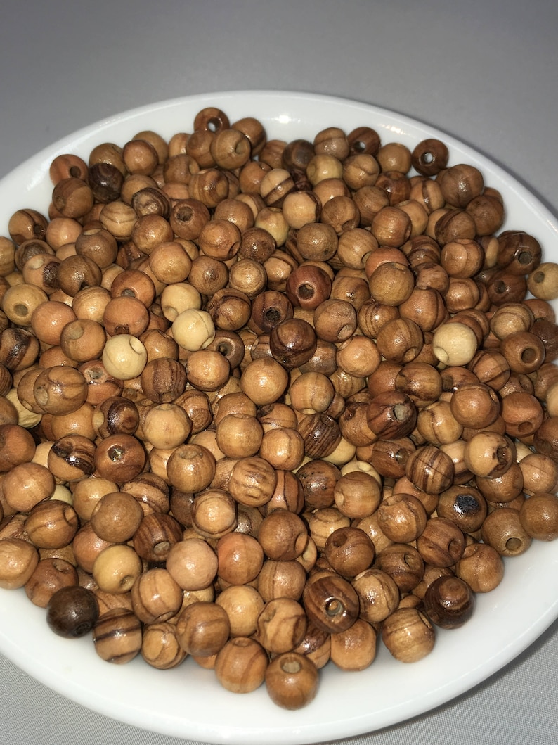 May include: A bowl filled with a large quantity of small, round, wooden beads. The beads are a light brown color with darker brown streaks.