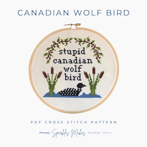 May include: A cross-stitch embroidery hoop with the text "CANADIAN WOLF BIRD" at the top. The design features a loon in water, cattails, and the words "stupid canadian wolf bird". The words "PDF CROSS STITCH PATTERN" and "Sparkles Makes Studio" are also included.