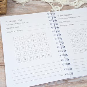 Puede incluir: Una agenda de espiral abierta en una p&aacute;gina titulada 30 DAY CHALLENGE. La p&aacute;gina incluye el texto Progress, not perfection, one day at a time, l&iacute;neas para Challenge Focus y Motivation/Reward, y una cuadr&iacute;cula de treinta casillas numeradas.