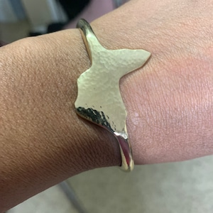 May include: A gold hammered metal cuff bracelet in the shape of a stylized bird.