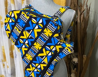 May include: A blue, yellow, and white patterned crossbody bag with a zipper closure. The bag has a geometric design and is worn on a mannequin.
