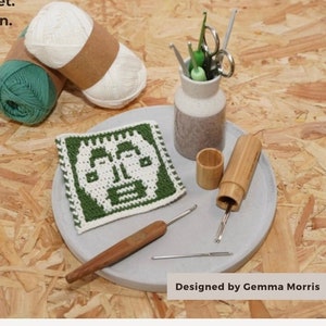 Könnte beinhalten: Ein Häkelmuster für einen quadratischen Untersetzer in Grün und Weiß mit einem Gesichtsdesign. Das Muster heißt "The Betty Square" und wurde von Gemma Morris entworfen.