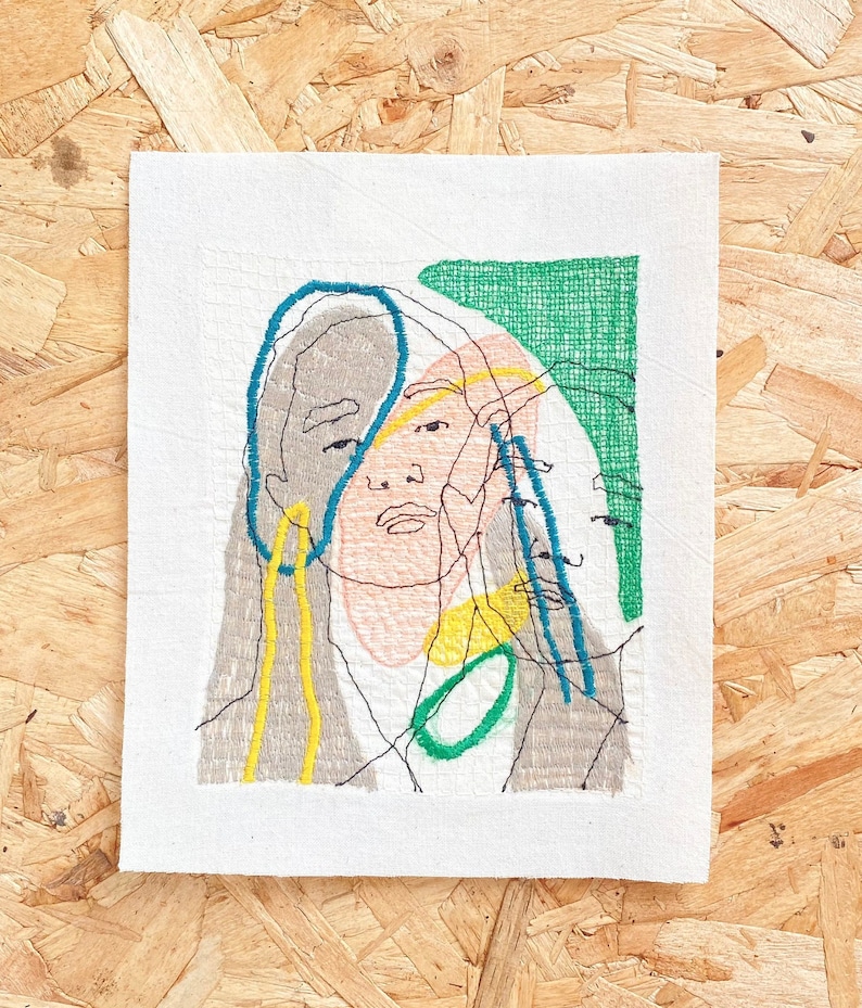 May include: Embroidered artwork featuring a stylized portrait of a person with a green, blue, yellow, and pink color scheme.