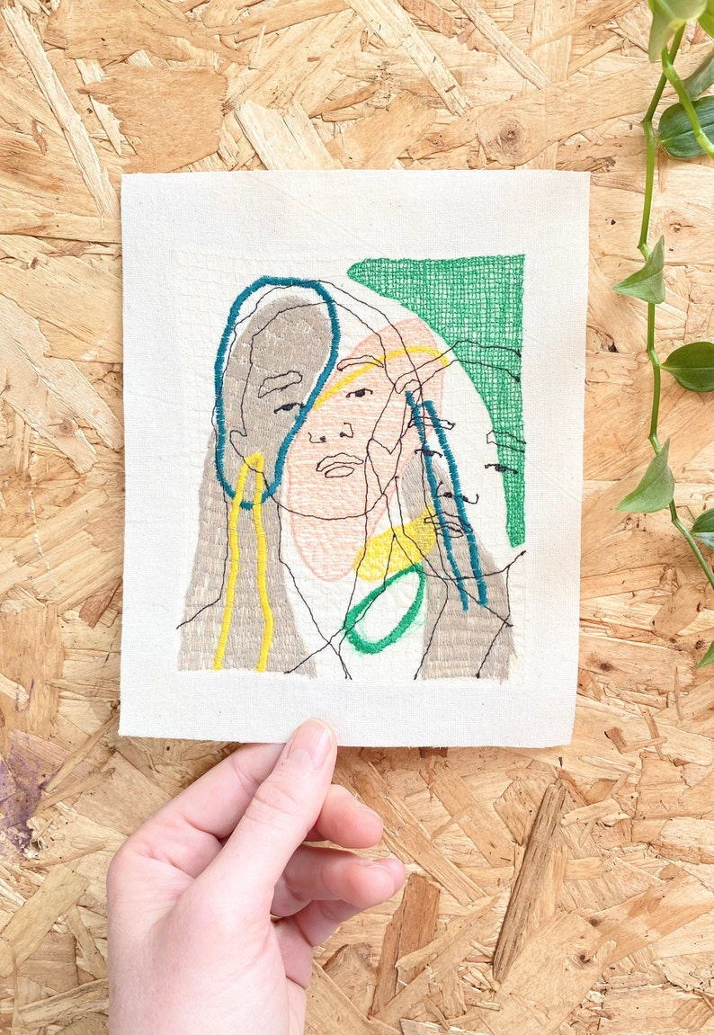 May include: Embroidered artwork featuring a stylized portrait of a person with overlapping lines and shapes in shades of green, blue, yellow, and brown.