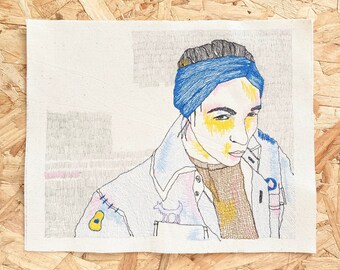 May include: Embroidered portrait of a person wearing a blue bandana and a light blue jacket with yellow accents. The person is looking down and has a serious expression.