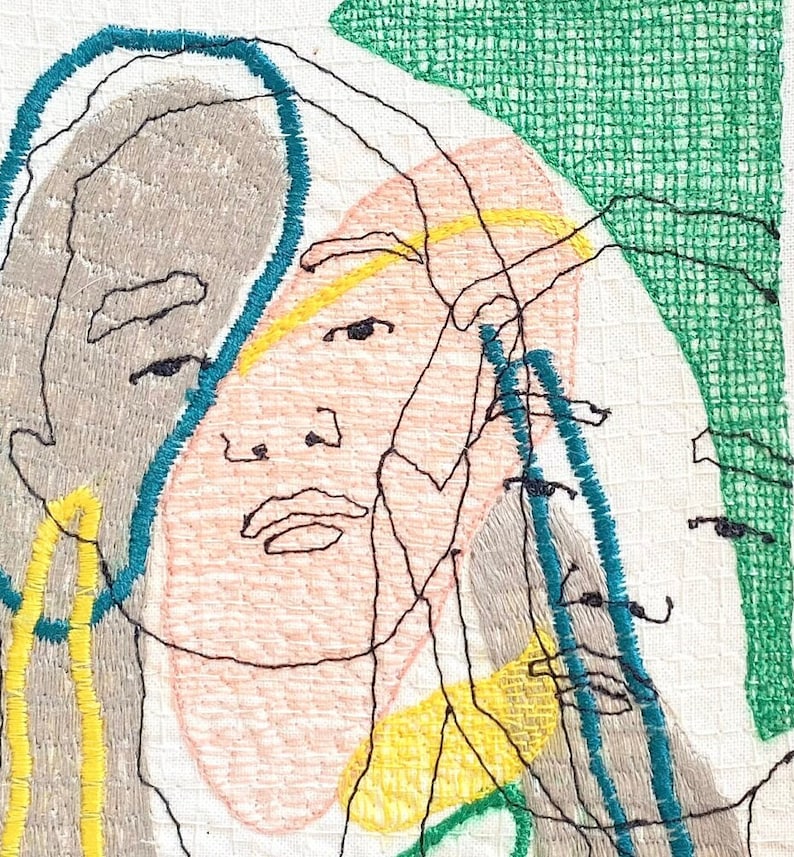 May include: Embroidered artwork featuring a stylized portrait of a person with multiple overlapping faces. The faces are outlined in black thread and filled with shades of pink, gray, and yellow. The background is a white fabric with a green grid pattern.