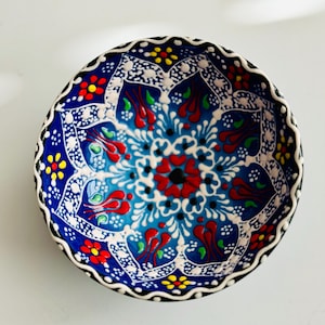 May include: A small, blue and white ceramic bowl with a colorful floral pattern. The bowl has a scalloped edge and is decorated with red, yellow, green, and blue flowers.