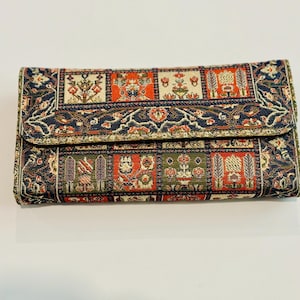 May include: A rectangular, patterned clutch with a flap closure. The fabric features a repeating design of floral and geometric elements in shades of red, green, and gold on a dark blue background. The clutch is closed.