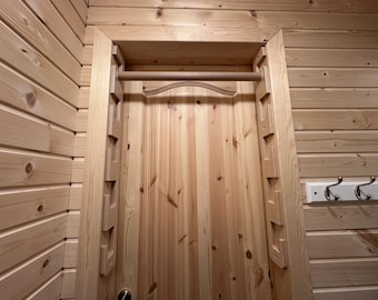 May include: Wooden door frame with a built-in clothes drying rack. The frame and rack are made of light-coloured wood, with a decorative curved design on the rack. The door is made of vertical wooden planks.