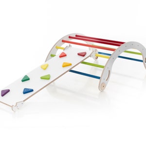May include: A wooden rainbow climber with a slide attached. The climber has five colorful rungs and the slide has a white surface with colorful triangle shapes.