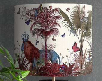 May include: A black lamp with a white lampshade featuring a jungle scene with a lion, palm trees, and butterflies. The lampshade has a red, green, and blue color scheme.