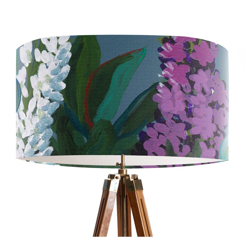 May include: A floor lamp with a white and blue floral patterned lampshade. The lampshade has a dark blue background with white and purple flowers. The lamp has a wooden tripod base.