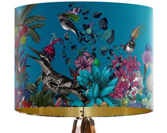 May include: A teal lampshade with a botanical design featuring colorful flowers and birds. The lampshade has a gold-colored interior and is supported by a wooden tripod base. The birds are black and white, and the flowers are pink, blue, and purple.