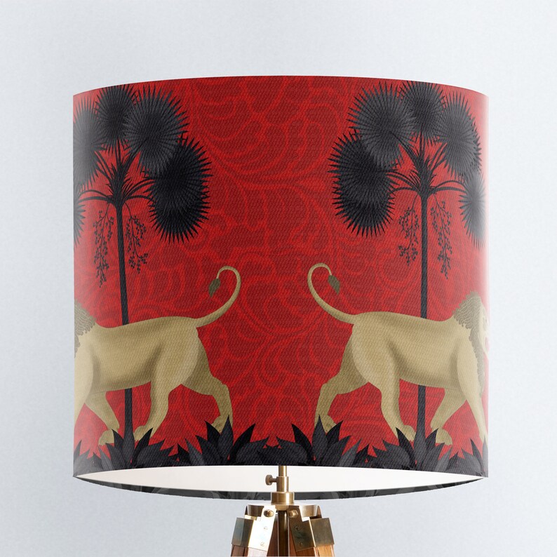 May include: Red lampshade featuring a black and gold lion design. The lions are walking through a jungle scene with palm trees.