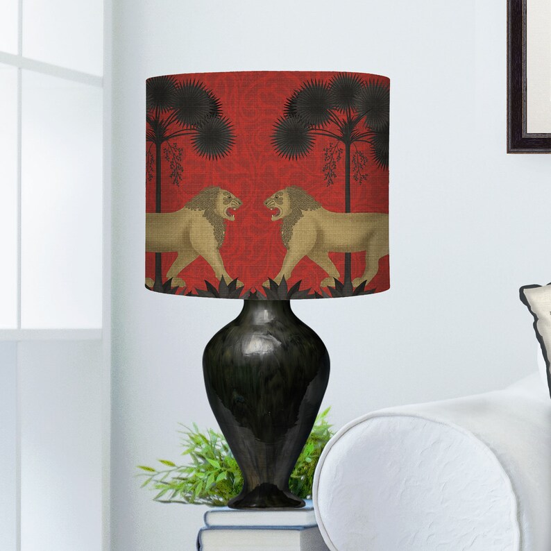 May include: A black lamp with a red and gold lampshade featuring a repeating pattern of lions and palm trees. The lampshade is made of fabric and has a textured surface.