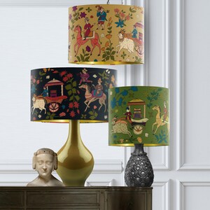 May include: Three table lamps with different colored lampshades featuring a colorful Indian-inspired design of people riding horses and pulling a carriage. The lampshades are black, gold, and green.