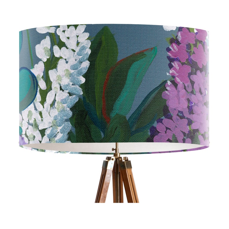 May include: A blue and green floral lampshade with white and purple flowers. The lampshade is on a tripod stand.