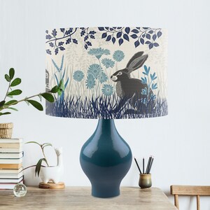 May include: A teal blue table lamp with a cream-colored lampshade featuring a black rabbit in a blue and green floral pattern.