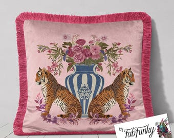 May include: Pink decorative throw pillow with a fringed edge. The pillow features a design of two tigers flanking a blue and white vase filled with flowers. The tigers are orange and black. The pillow has a pink background.