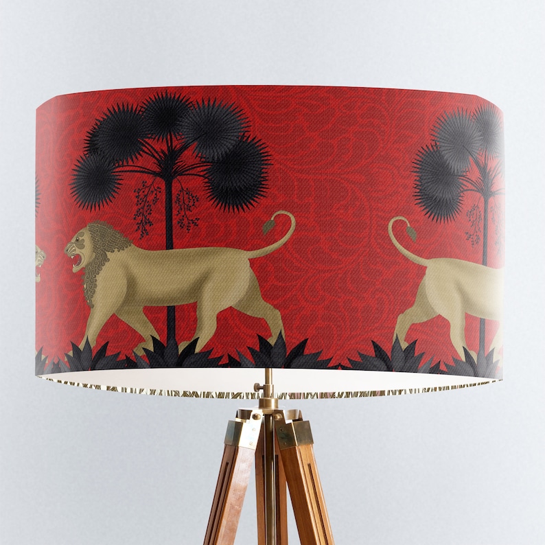 May include: A red lampshade with a repeating pattern of black palm trees and gold lions. The lampshade is on a wooden tripod stand.
