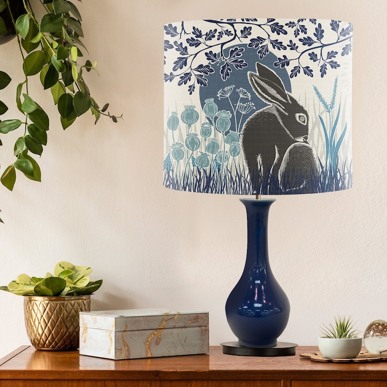 May include: A blue ceramic table lamp with a white lampshade featuring a black rabbit illustration in a blue and white floral pattern.