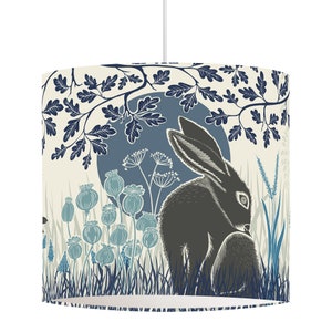 May include: A cream-colored lampshade with a blue and black illustration of a rabbit sitting in a field of flowers and grass under a blue moon. The design is stylized and features a repeating pattern of leaves and branches.