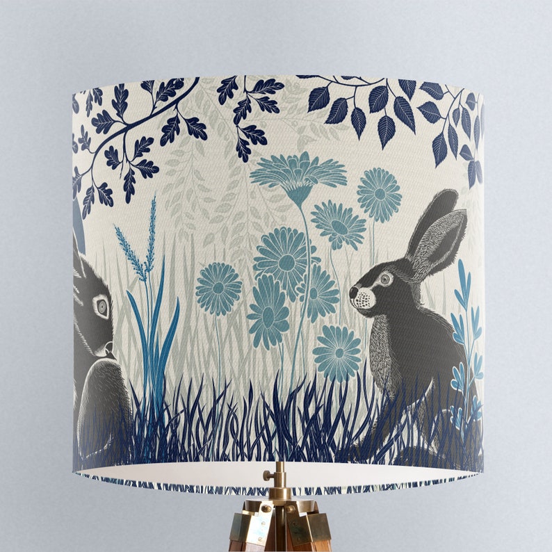 May include: A lampshade with a cream background and a blue and black floral pattern. The pattern features stylized flowers, leaves, and two rabbits.