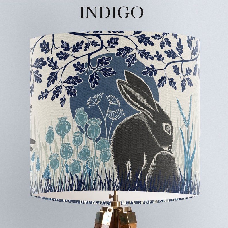 May include: A lampshade with a blue and white design featuring a black rabbit in a forest setting. The design includes leaves, flowers, and a moon.