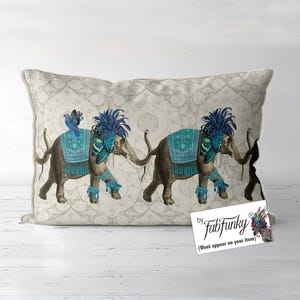 May include: Rectangular decorative pillow featuring two elephants adorned with teal and blue accents. The elephants are depicted with ornate headdresses and blankets, and a bird perched on one. The pillow has a patterned background.