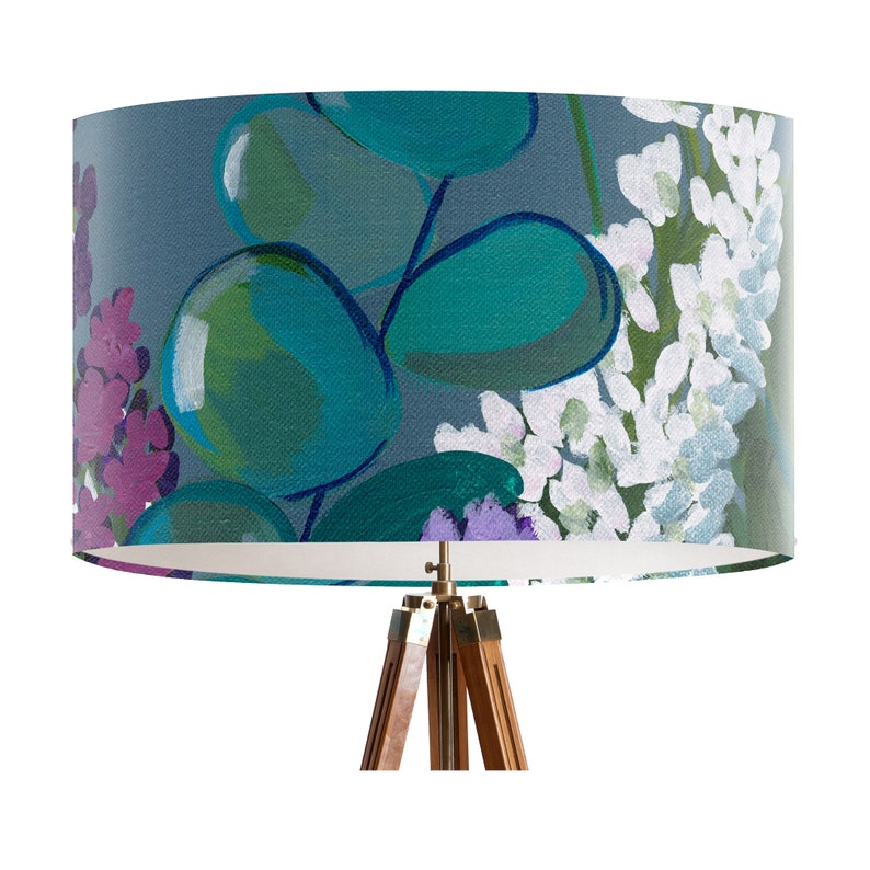 May include: A gray lampshade with a floral pattern featuring teal, green, purple, and white flowers. The lampshade is on a tripod stand with a wooden base.