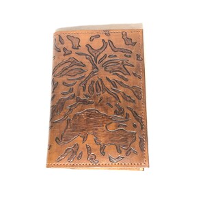 May include: A brown leather wallet with an embossed design featuring a central floral motif and animal figures. The wallet is rectangular and has a stitched border. The leather has a natural, aged appearance.